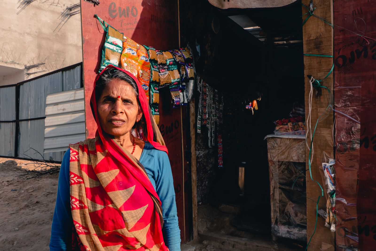 An older woman in a sari standing outside a neighbourhood shop in India